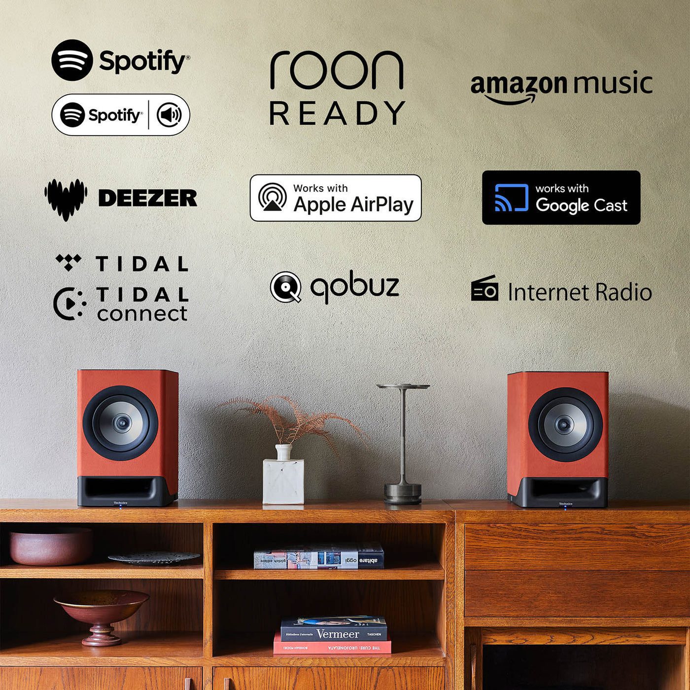 Altavoces Technics CX700 en una mesa de consola en un entorno de sala de estar con varios logotipos para compatibilidad: Spotify, Roon Read, Amazon Music, funciona con Google Cast, radio por Internet, Qobuz, Tidal, Tidal Connect, Deezer
