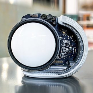 Reloj de pulsera redondo plateado abierto visto desde el interior, esfera blanca con circuitos impresos negros, correa metálica articulada